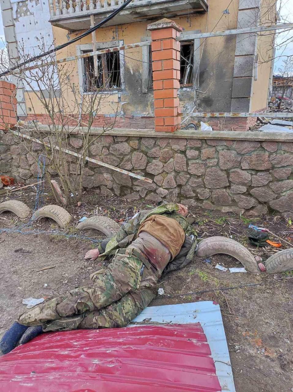 The corpse of a Russian military against the background of a destroyed house