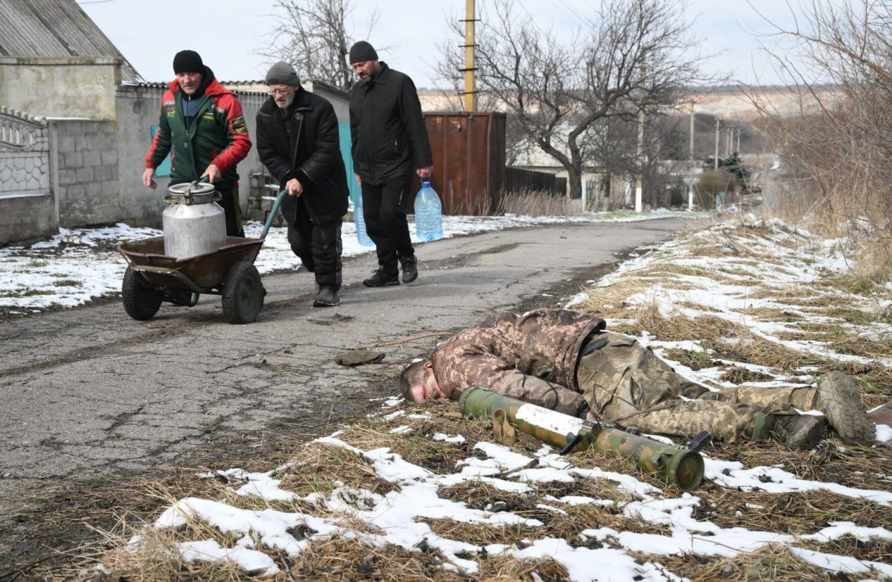 Elderly men fetch water against the background of a military corpse with a grenade launcher