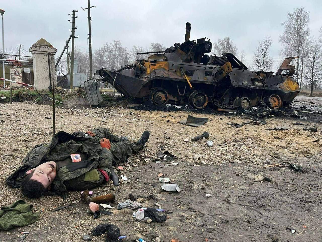 The corpse of a Russian soldier against the background of a burnt armored personnel carrier